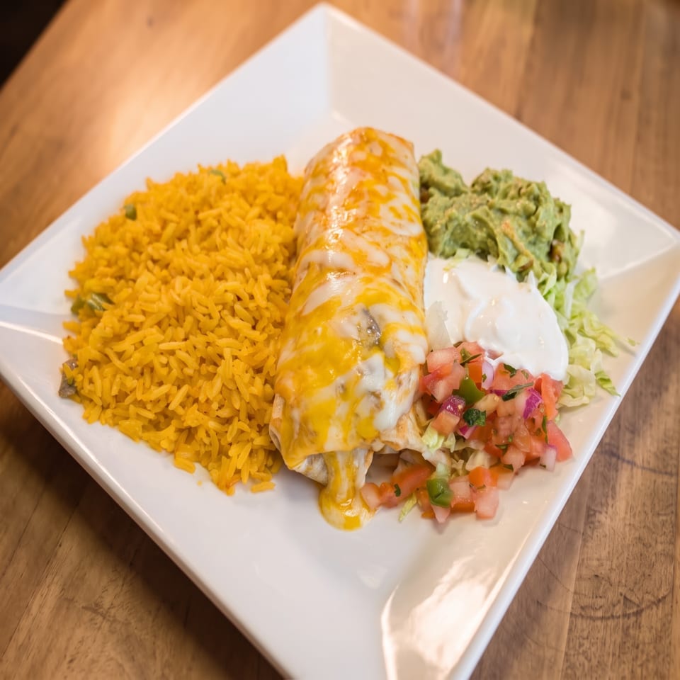 Cheesy enchilada served with yellow rice, guacamole, sour cream, pico de gallo, and lettuce on a white plate.