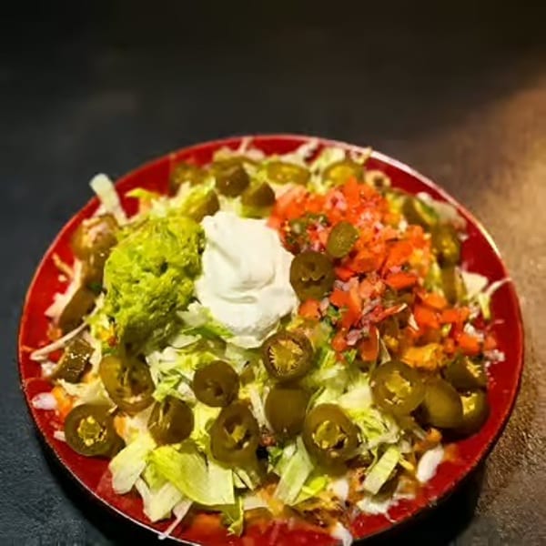 Loaded nachos topped with lettuce, guacamole, sour cream, diced tomatoes, cheese, and sliced jalapeños on a red plate.
