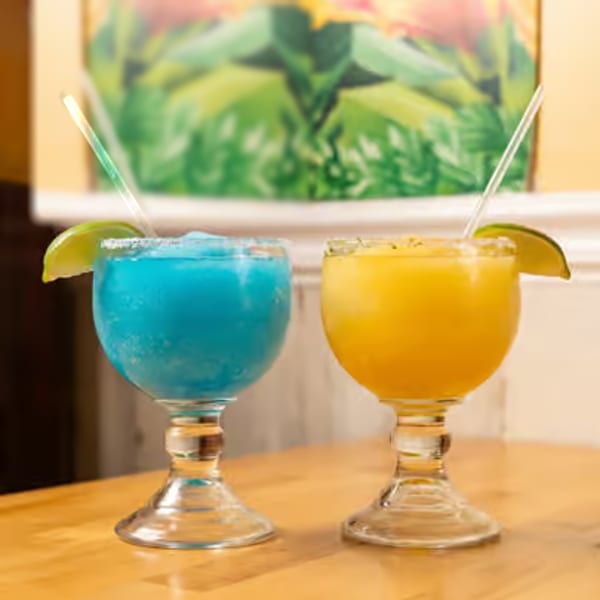 Blue and orange frozen cocktails with lime garnishes and straws on a restaurant table.