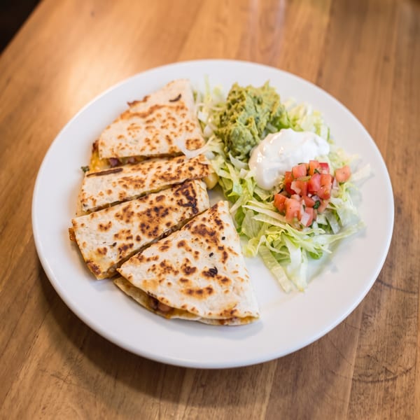 Quesadilla slices with guacamole, sour cream, pico de gallo, and shredded lettuce on a white plate.