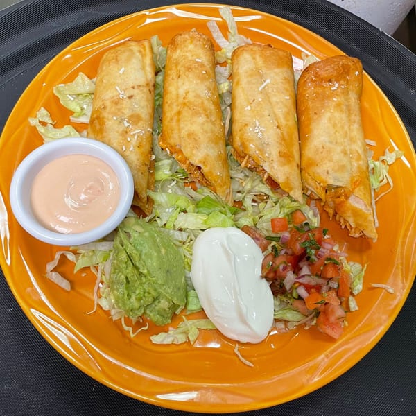 Four crispy rolled tacos served over lettuce with guacamole, sour cream, pico de gallo, and creamy dipping sauce on an orange plate.