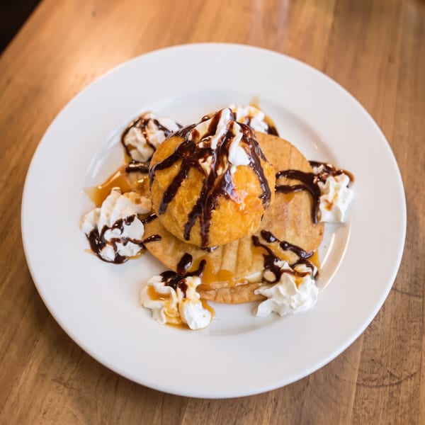 Fried ice cream dessert with whipped cream, chocolate, and caramel drizzle on a white plate.